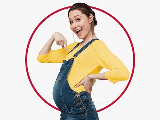 Glad ung gravid kvinna i gul jumper som pekar på sin mage